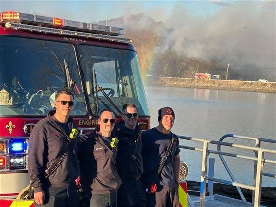 Four firefighters next to fire truck next to reservoir
