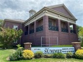 image of brick summit city hall building from outside with the white sign in front that reads city hall city of summit municipal offices police department. there are grass and plants in front of/around the building