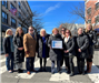 image of group of people standing in a crosswalk downtown holding an award posing for a photo