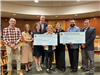 image of group of people holding large checks in council chamber posing for a photo