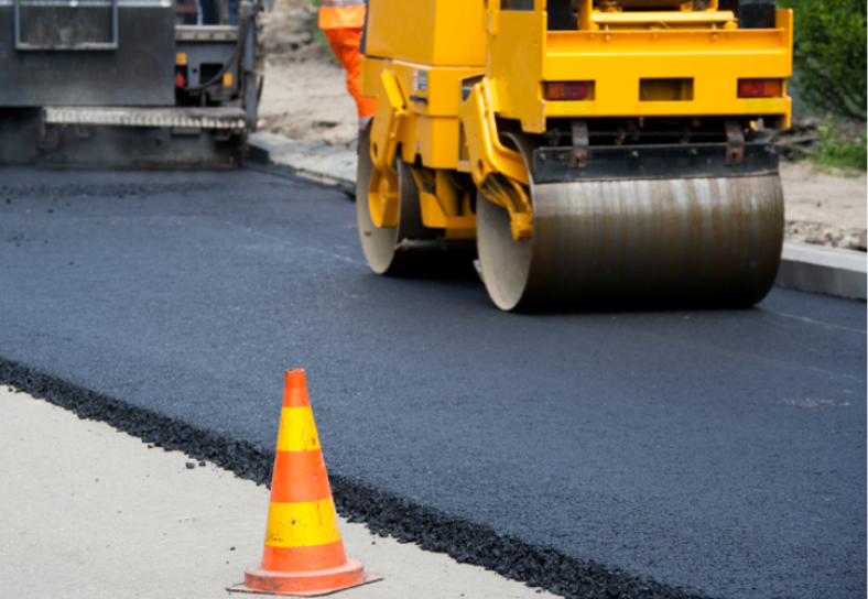 image of paving truck on a partially paved road with an orange cone in the front