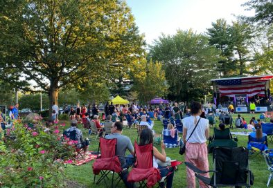large group of people gathered in grassy park area with stage and bang in background