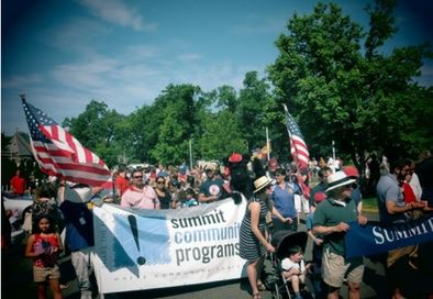 people marching in parade with banners and signs with blue sky above and green trees in background