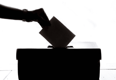 black and white image of hand placing ballot into voting box