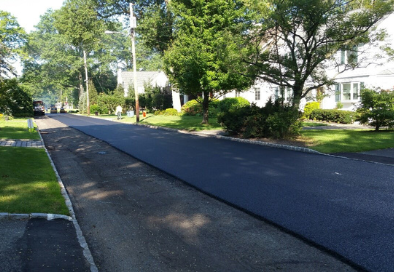 image of road getting paved, there are houses and trees in the background