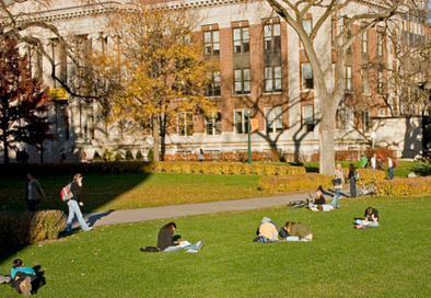 image of college campus with building in the back, students sitting on the quad and studying