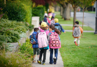 image from behind of children with backpacks walking on a sidewalk