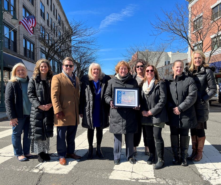 image of group of people standing in a crosswalk downtown holding an award posing for a photo