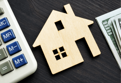 image of small wooden house on a table with a calculator and dollar bills